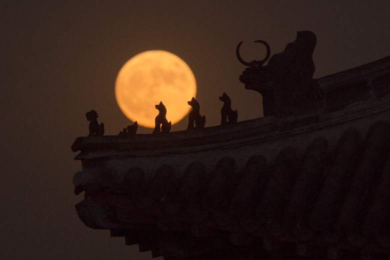 Una "superluna" se levanta detrás de pequeñas esculturas que se colocan en el tejado de una torre en la ciudad prohibida en Pekín el 14 de noviembre de 2016. (Getty)