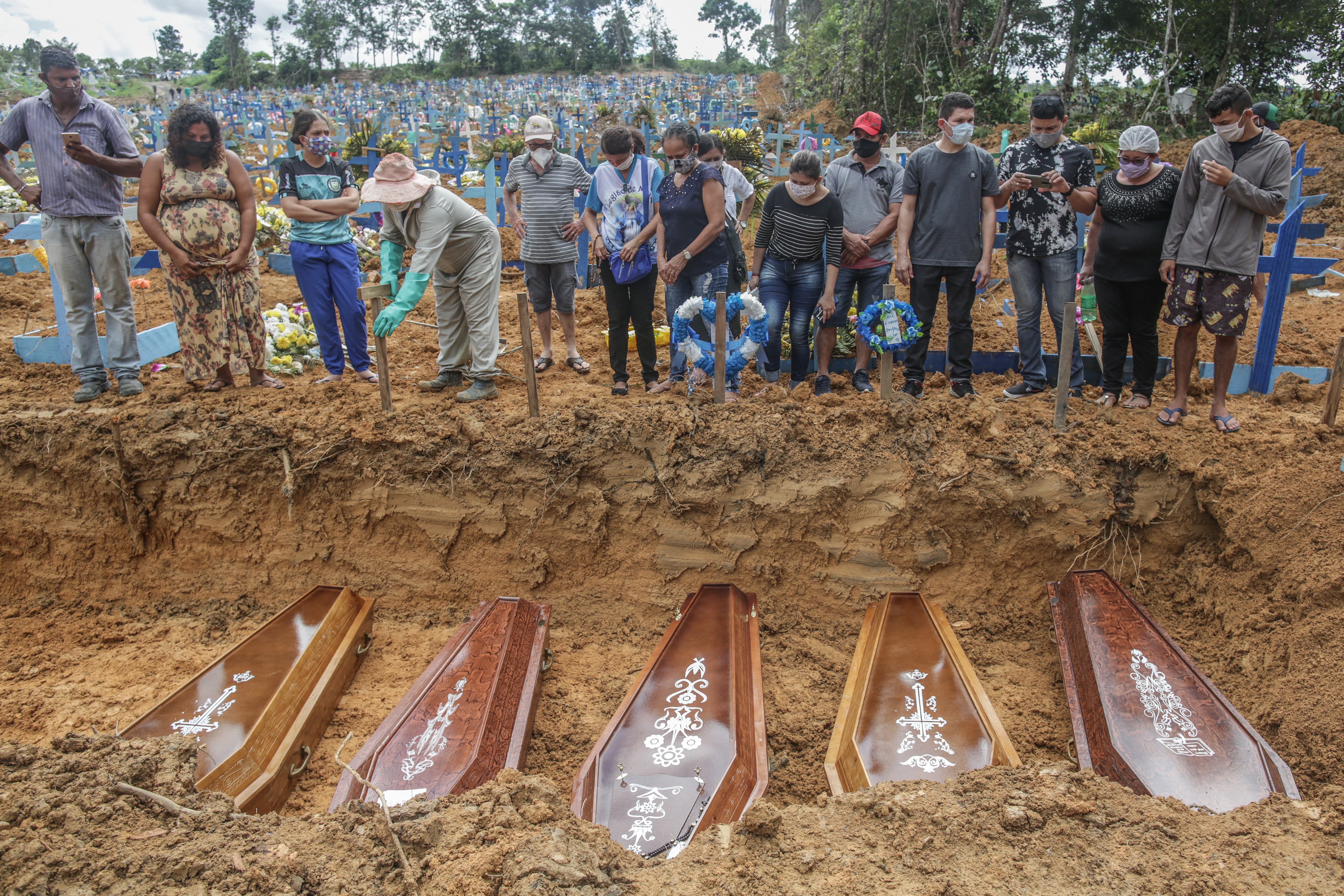 Personas con máscaras protectoras observan las tumbas con los restos de sus familiares durante un entierro masivo de las víctimas de la pandemia del coronavirus (COVID-19) en el cementerio Parque Taruma el 19 de mayo de 2020 en Manaus, Brasil.