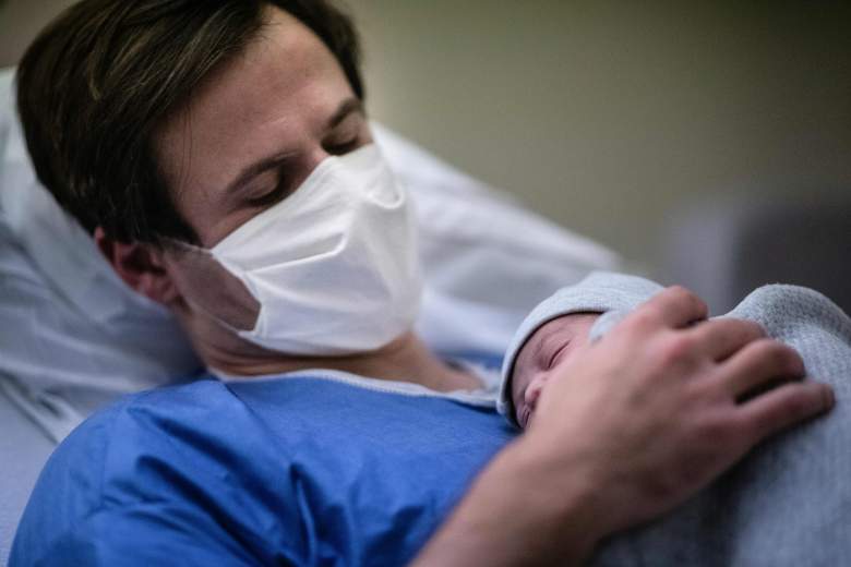 Un padre con máscara protectora sostiene a su hijo recién nacido contra su pecho durante la pandemia Covid-19