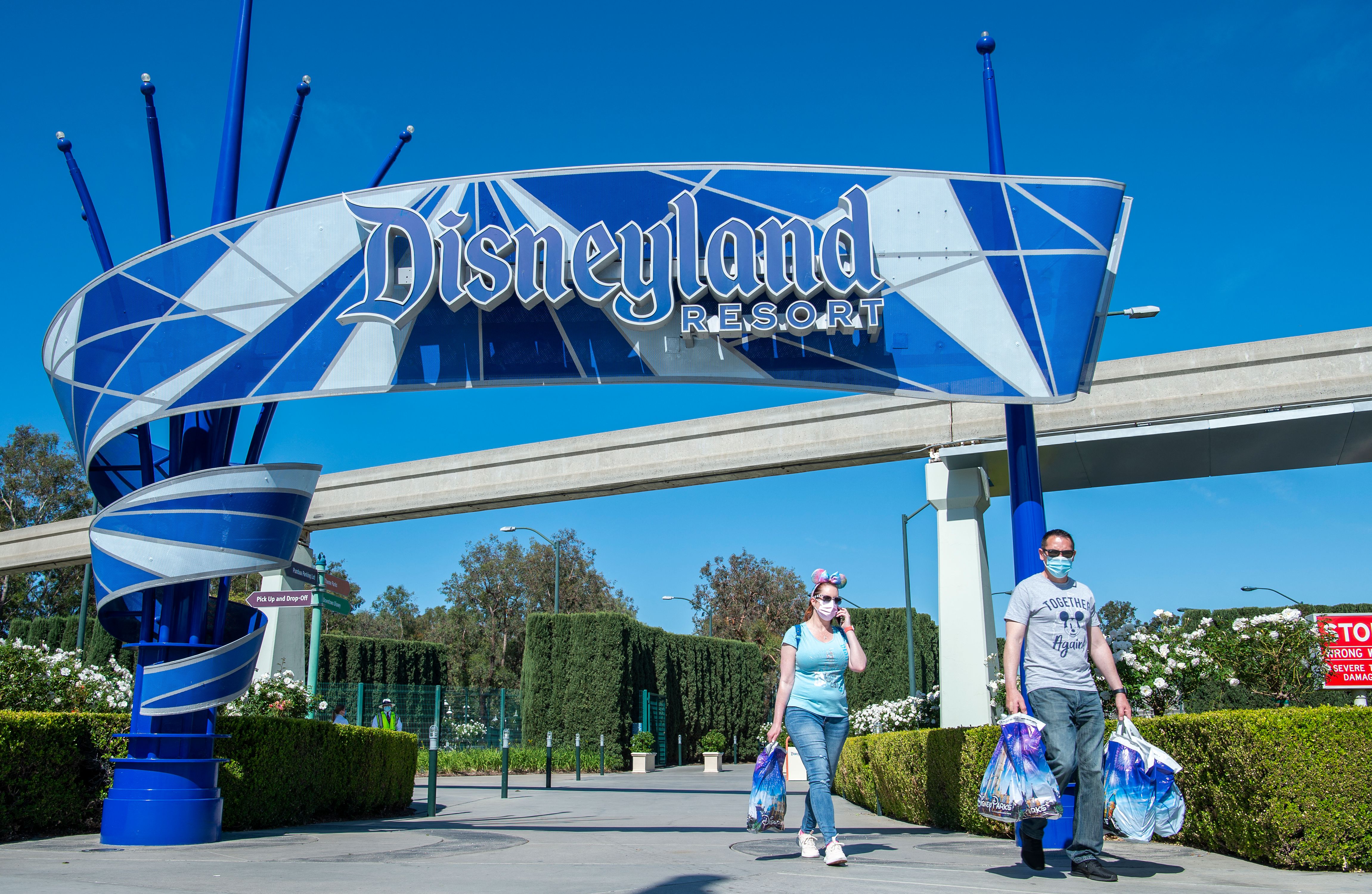 Los visitantes que llevan bolsas de Disney salen de Disneyland el día de la reapertura del parque el 30 de abril de 2021, en Anaheim, California, después de que se cerró en marzo de 2020 debido a la pandemia de Covid-19