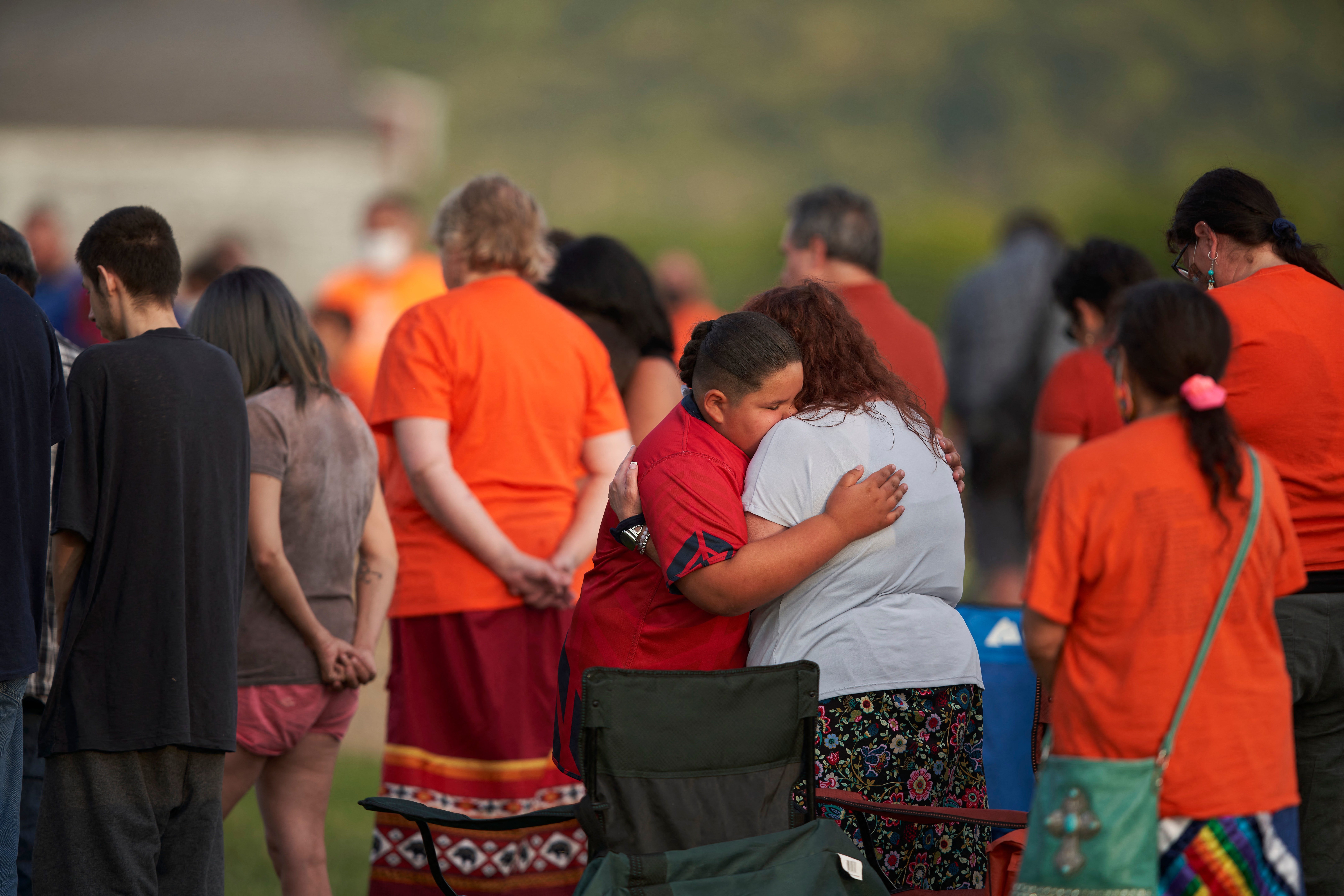 La gente se abraza durante una vigilia en un campo donde se encontraron restos humanos en tumbas sin marcar en el sitio de la antigua Escuela Residencial Indígena Marieval en la Primera Nación Cowessess en Saskatchewan el 26 de junio de 2021.