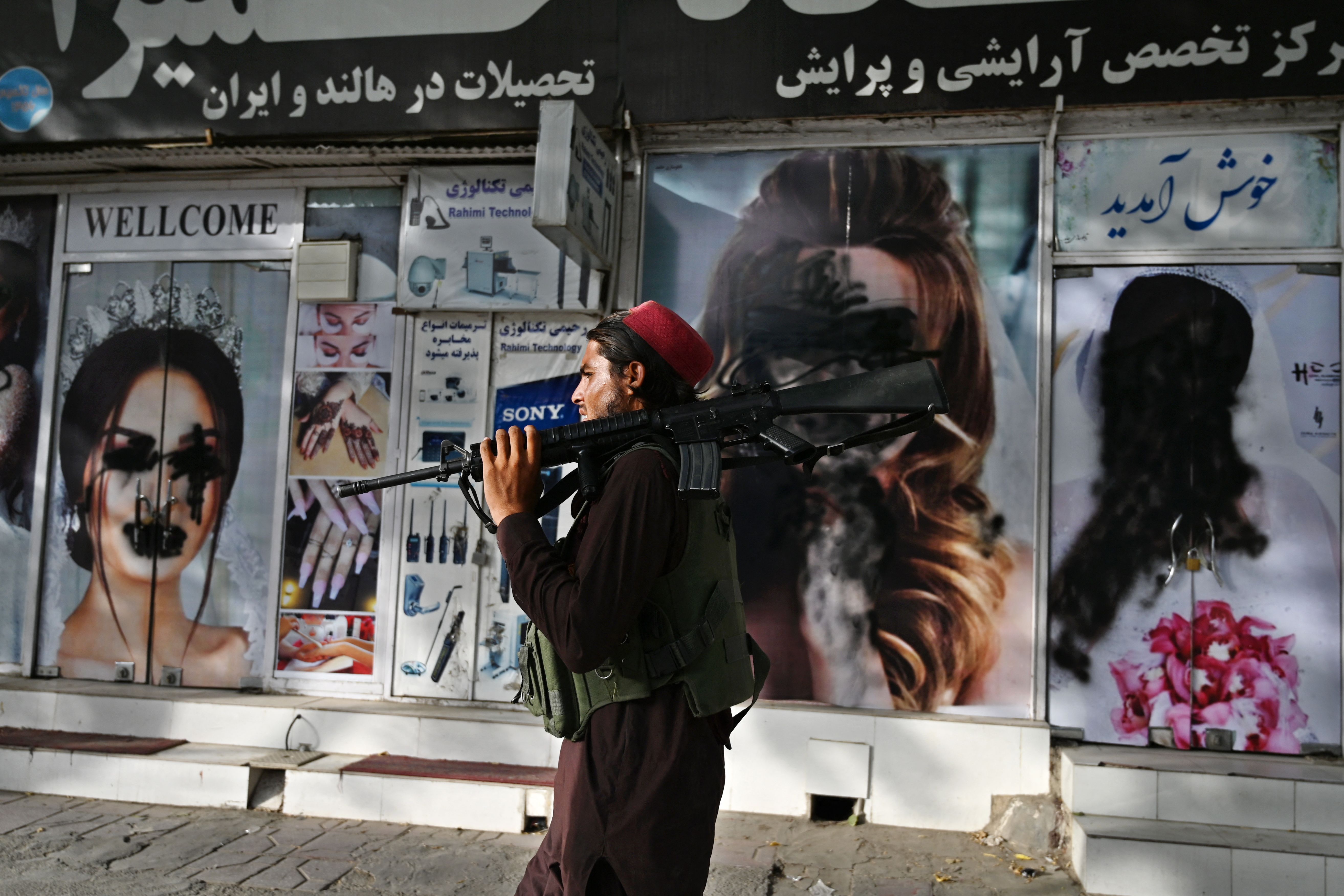 Un combatiente talibán pasa frente a un salón de belleza con imágenes de mujeres desfiguradas con pintura en aerosol en Shar-e-Naw en Kabul el 18 de agosto de 2021