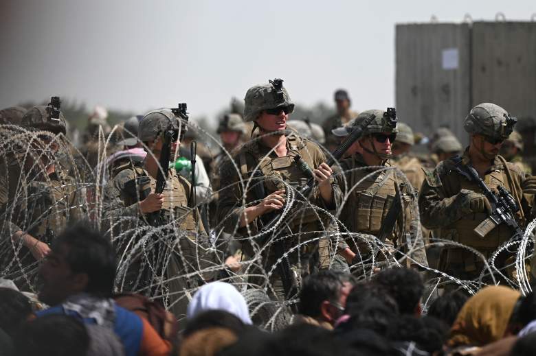 Los soldados estadounidenses montan guardia detrás de un alambre de púas mientras los afganos se sientan en una carretera cerca de la parte militar del aeropuerto en Kabul el 20 de agosto de 2021, con la esperanza de huir del país después de la toma militar de Afganistán por los talibanes.