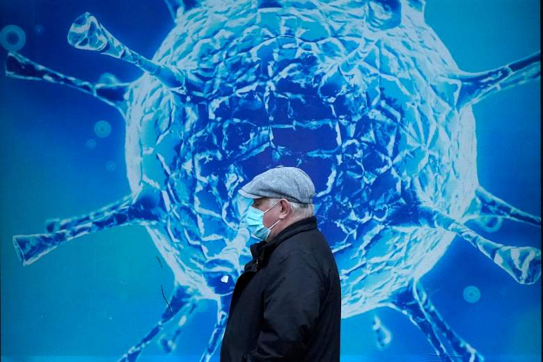 Un hombre con una máscara protectora pasa junto a una ilustración de un virus