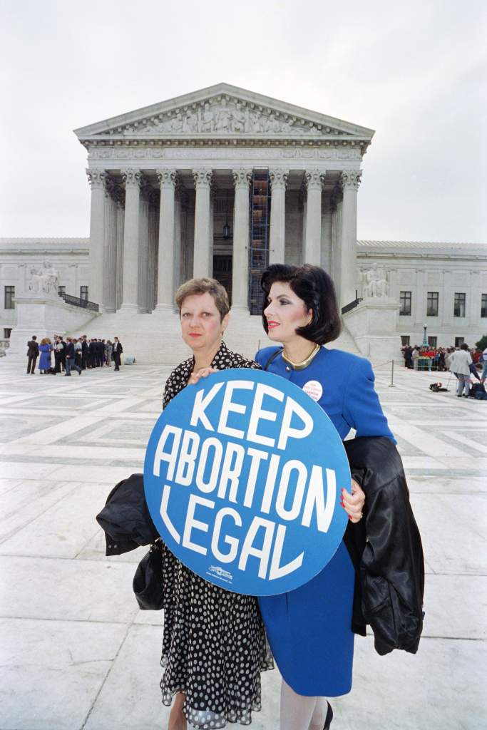 Norma Mc Corvey (izquierda), conocida como "Jane Roe" de la decisión de la Corte Suprema de 1973 Roe v. Wade, que legalizó el aborto, sostiene un cartel a favor del aborto con su abogada, Gloria Allred (derecha) frente al edificio de la Corte Suprema el 26 de abril de 1989, en Washington.