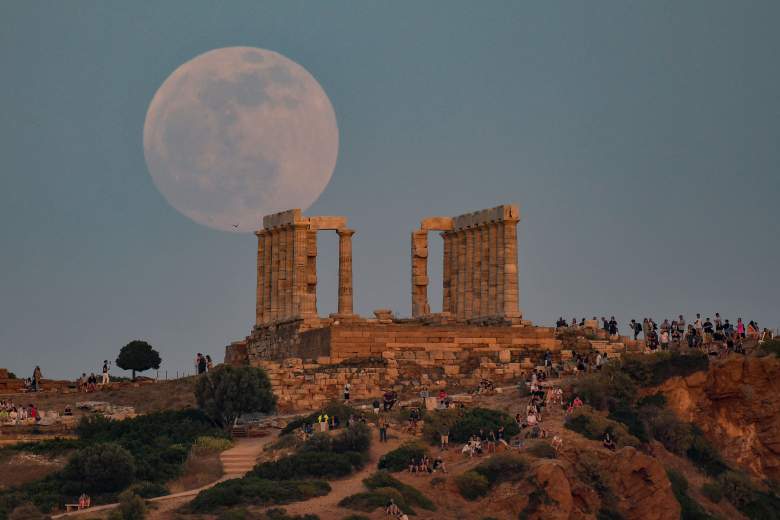 Los lugareños y los turistas observan la salida de la luna por el Templo de Peseidon en el cabo de Sounion, a unos 70 km al sur de Atenas el 15 de mayo de 2022.